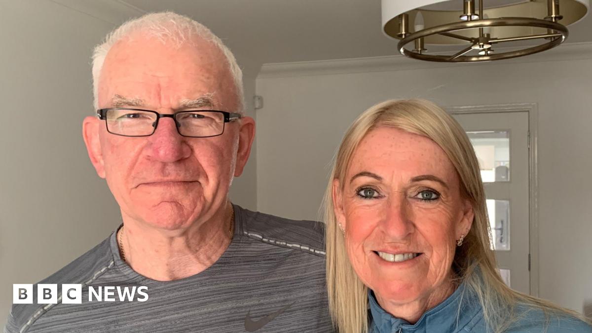 Chris and Rosie McGrane stand together in their house looking into the camera.
