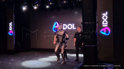 Robot dancing on stage in front of a screen displaying the word "IDOL."
