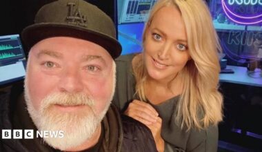 A middle aged man with a black baseball cap and grey beard and a blonde-haired younger woman smile at the camera
