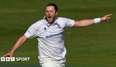 Sussex bowler Ollie Robinson celebrates a wicket with both arms out wide pointing, shouting, wearing club whites and sussex crest, with white wrist band on left wrist partially coveri ng siver bracelet