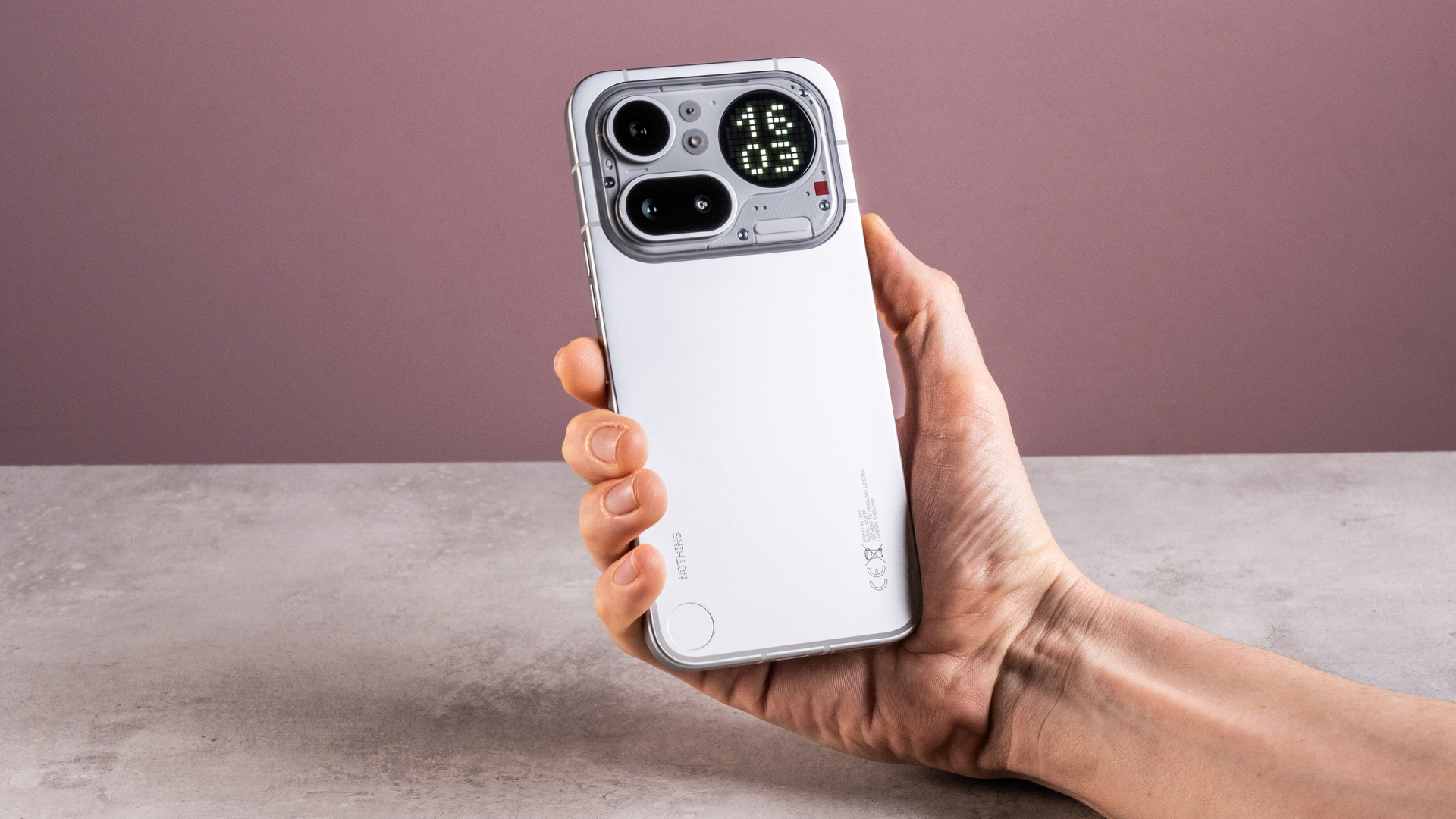 A man's hand holding the Nothing Phone (4a) Pro showing its aluminum unibody, camera module and Glyph Matrix, which features a digital clock reading '16:03'.