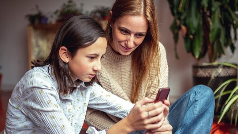 A high school aged girl and her mom looking at her phone.