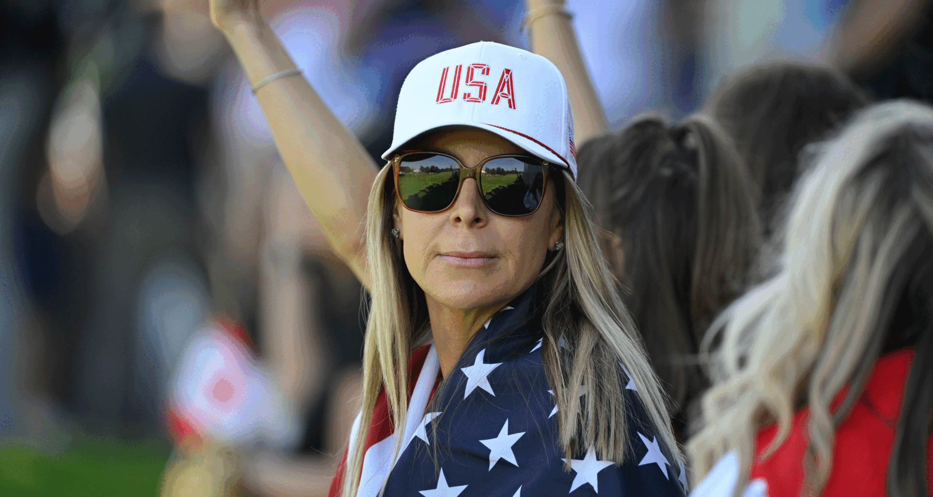 Brandt Snedeker's wife Mandy looks on through sunglasses at the 2024 Presidents Cup while wearing a Team USA cap and with a a US flag wrapped around her