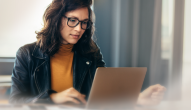Woman with glasses and dark hair sitting in front of computer.
