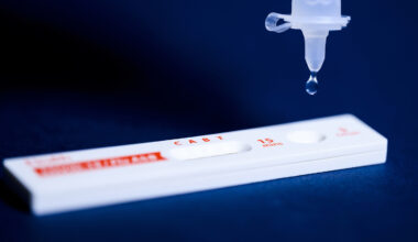 A COVID-19 test lying flat with a droplet falling from a syringe.