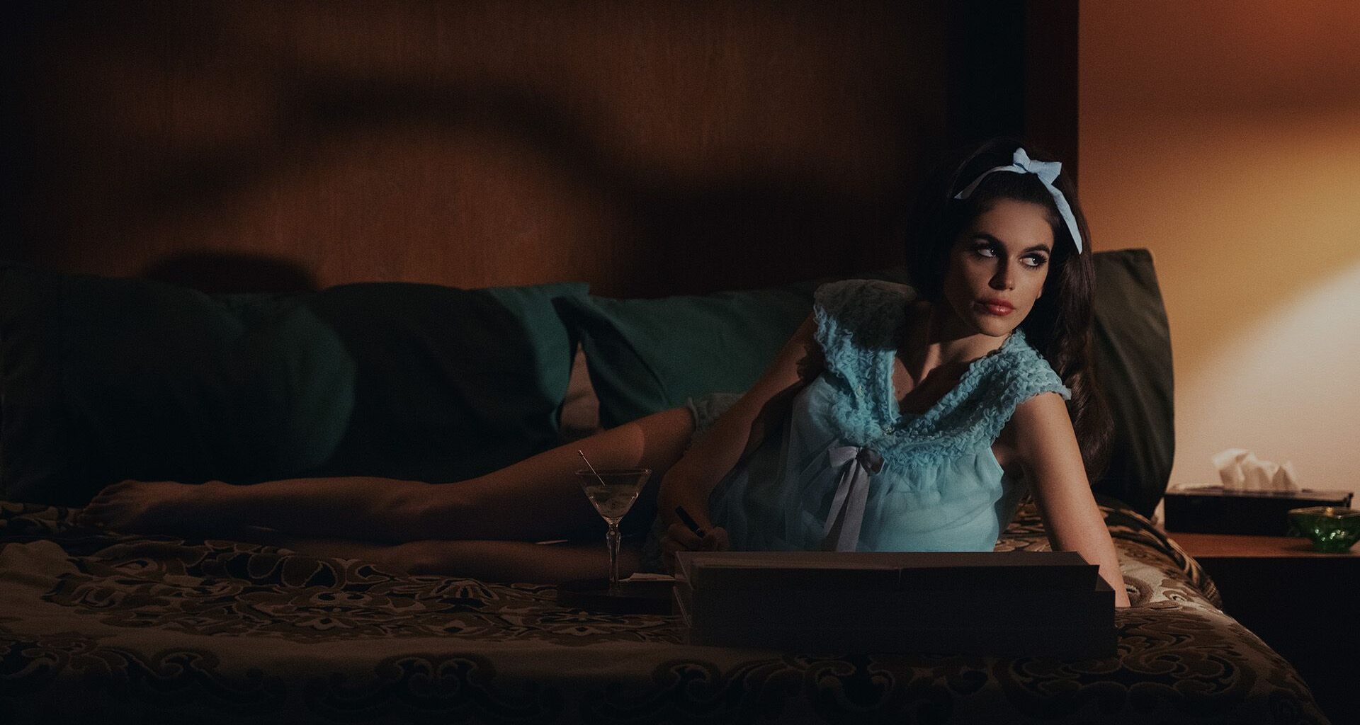 Kaia Gerber as Mitzi, reclining on a sofa, in Palm Royale season 2.
