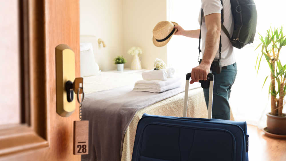 A person placing a sun hat on the hotel bed.