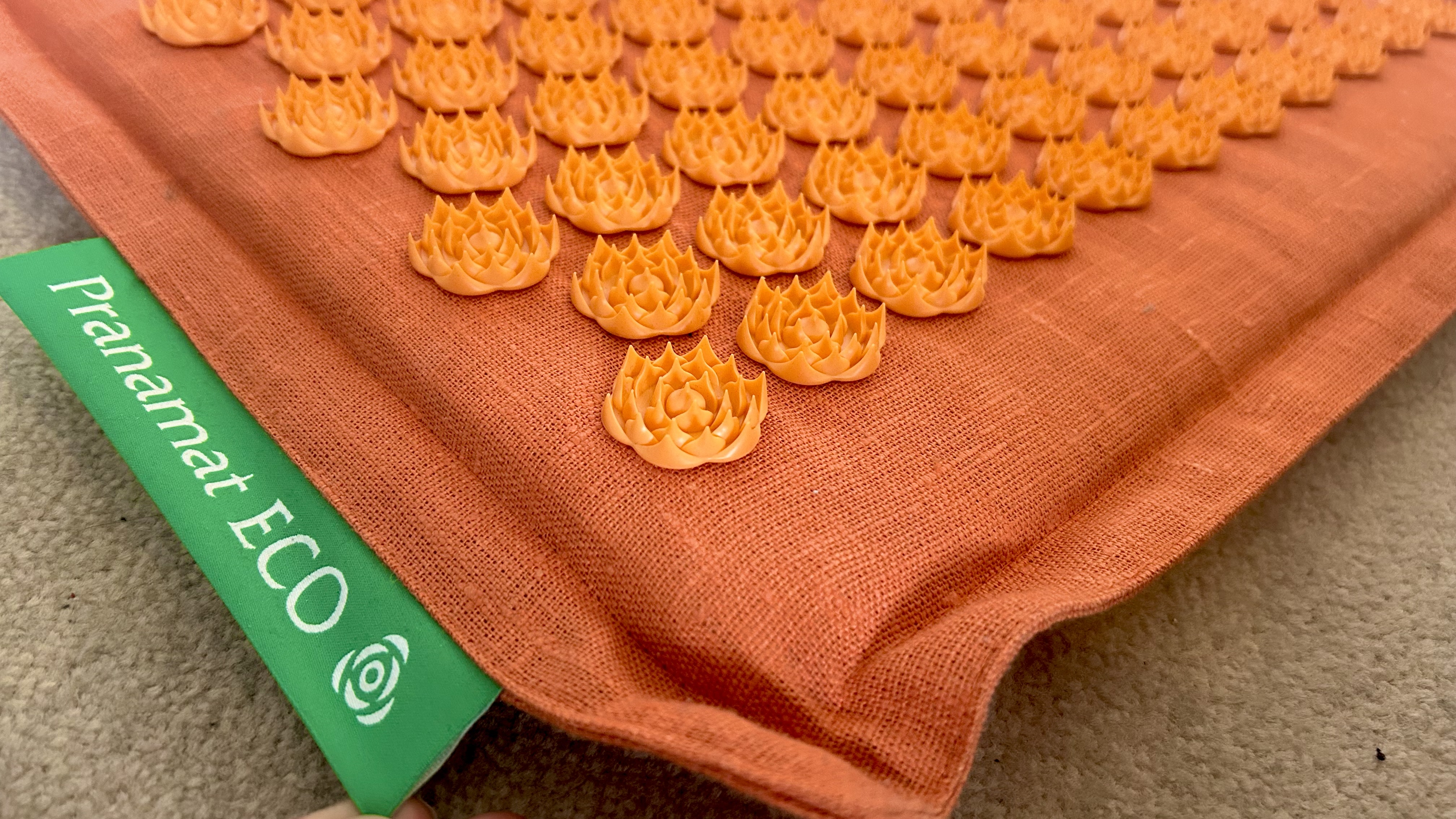 A close up of the Pranamat rug, showing orange material and spikes, as well as a green label reading Pranamat Eco