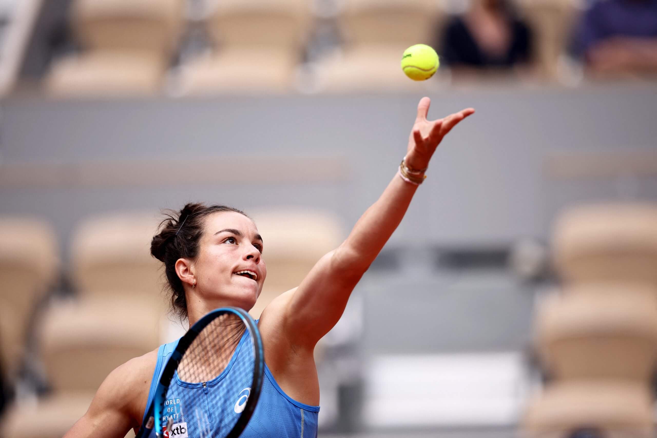 Loïs Boisson throws a tennis ball in the air with her left hand.