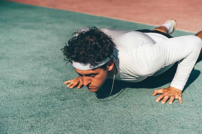 A sportsman doing push-ups, wearing a white long-sleeved tshirt and black shorts.