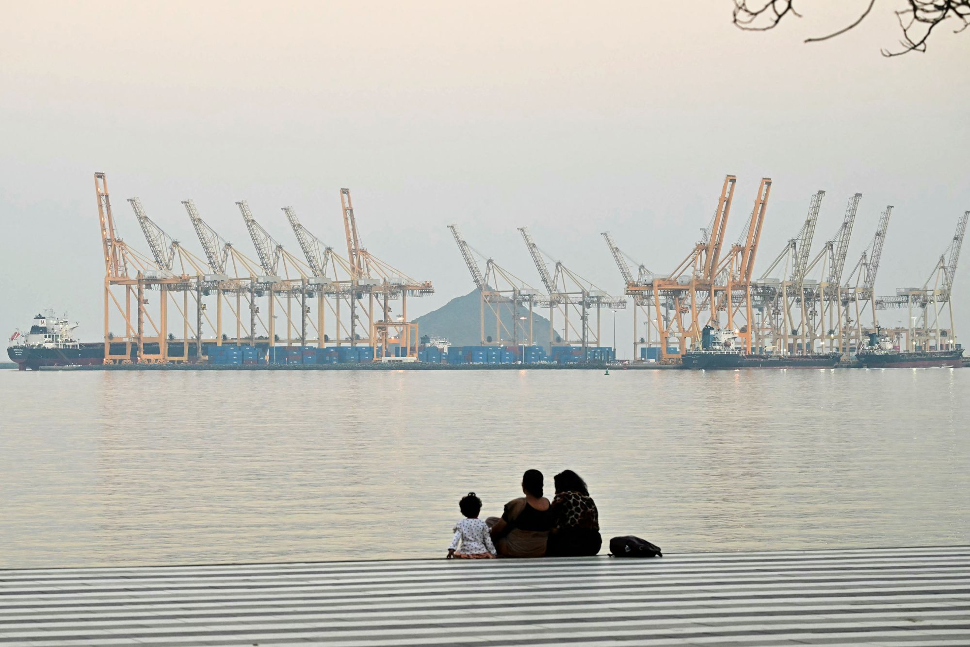 A family sits against the backdrop of a dockyard off coast city of Fujairah, in the Strait of Hormuz