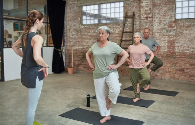 Female coach teaching yoga to seniors at gym