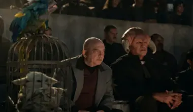 Grogu imprisoned in a birdcage next to Imperial warlord watching some entertainment with an Iktotchi