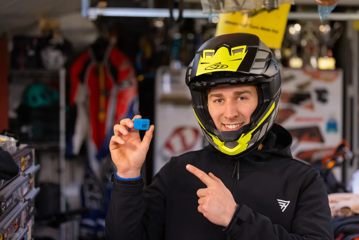 Rider wearing a full-face helmet holding a blue HIT head-impact sensor and pointing at it