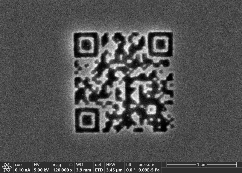 A grayscale microscope image showing a QR code in the black and white with a 1 micrometer scale bar at the bottom right for reference.