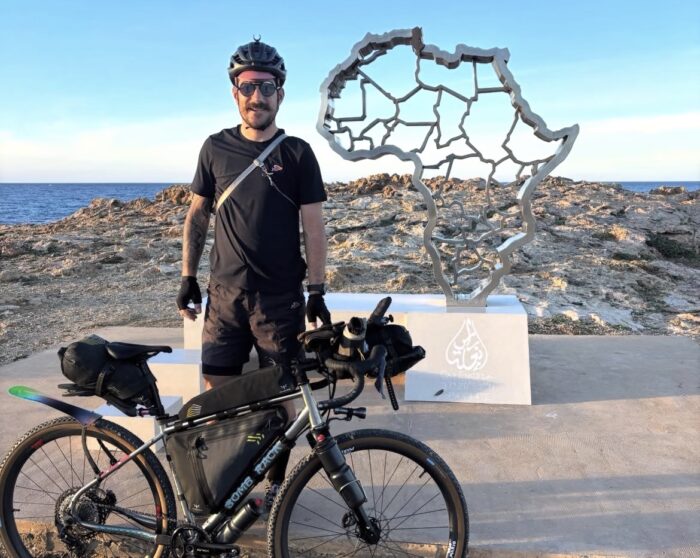 Swiss cyclist Adrien Liechti standing with his bike at Cape Angela in Tunisia.