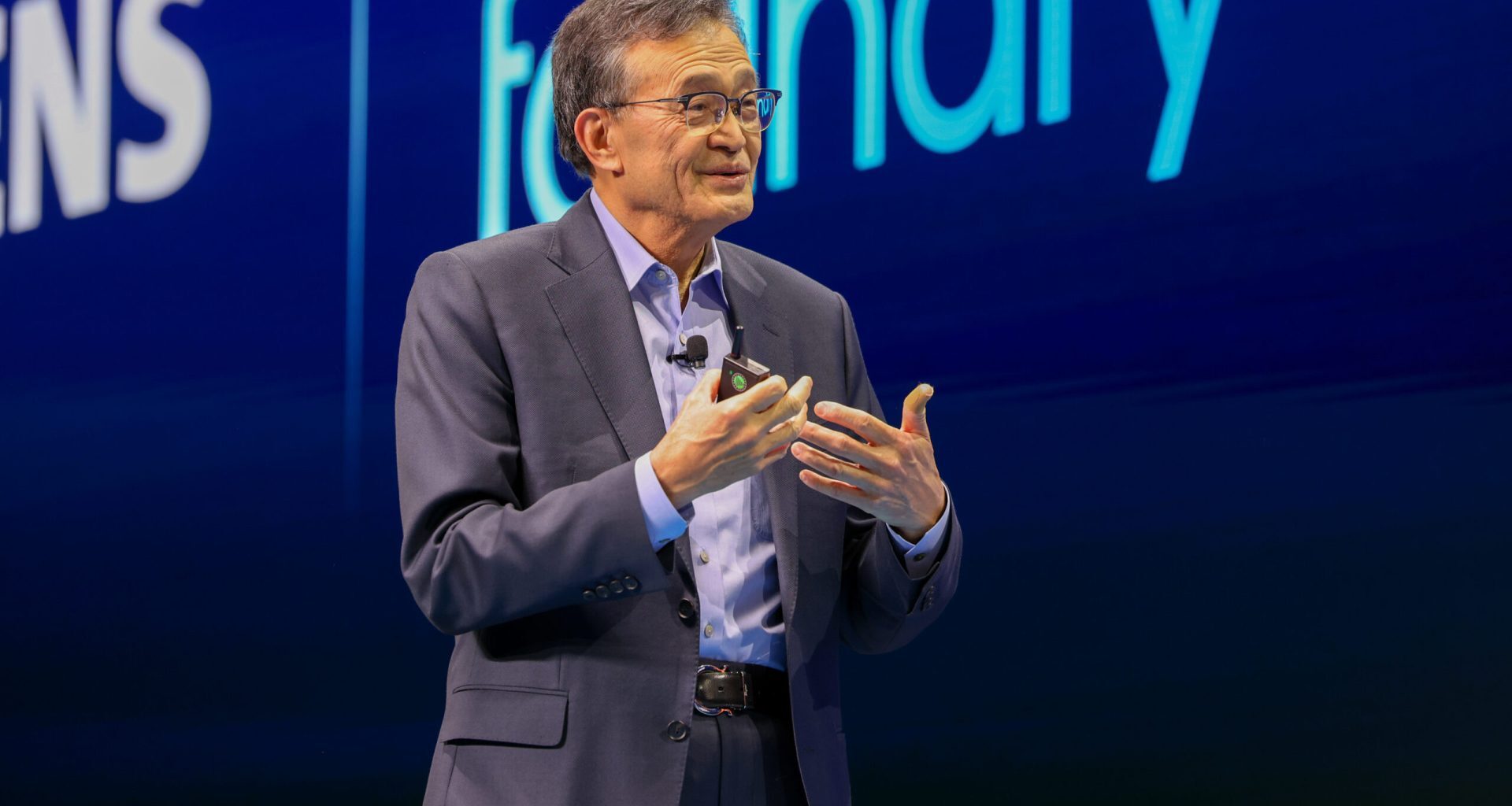 Man speaking on stage with Siemens and foundry visible in the background.