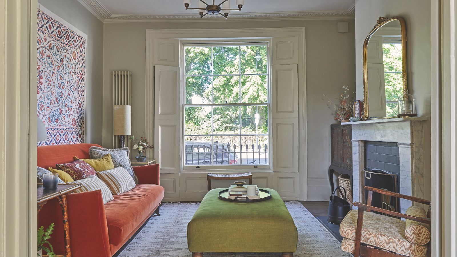 Living room with bay window, marble fireplace, orange sofa, tapestry and green ottoman