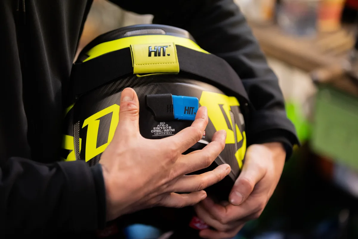 Hands attaching a HIT head-impact sensor to the rear of a full-face helmet