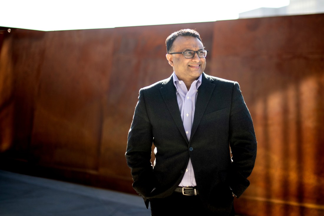 A portrait of Neil Maniar walking on the red pedestrian bridge on the Boston campus.
