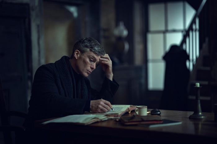 Cillian Murphy as Tommy in Peaky Blinders: The Immortal Man sat at a desk writing and reading.