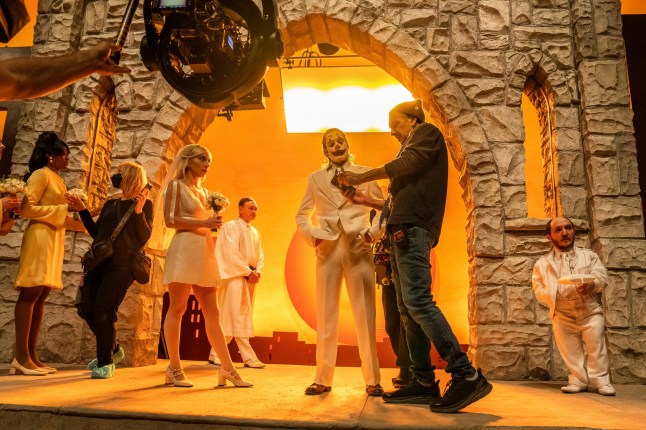 This image released by Warner Bros. Pictures shows actors Lady Gaga, left, and Joaquin Phoenix, center, on the set with filmmaker Todd Phillips during the filming of 