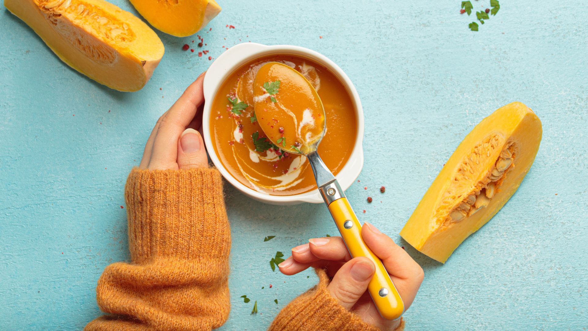 a woman's hands holding a bowl of squash soup with butternut squash slices scattered on the table