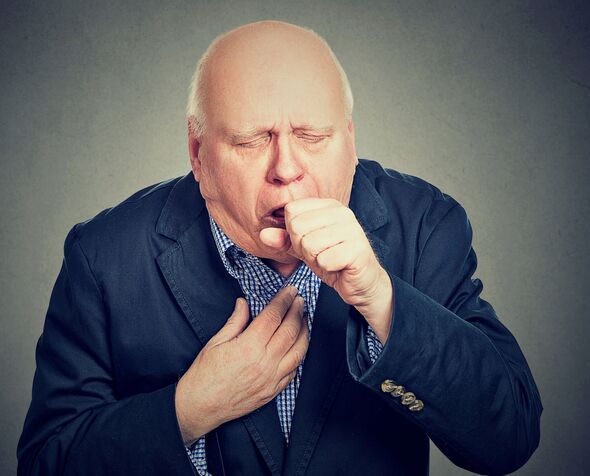 Old man coughing holding fist to mouth isolated on gray background