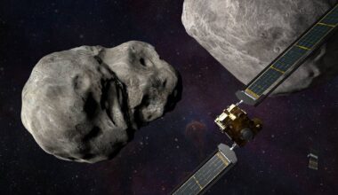 A box-shaped spacecraft with solar wings approaching two space rocks.