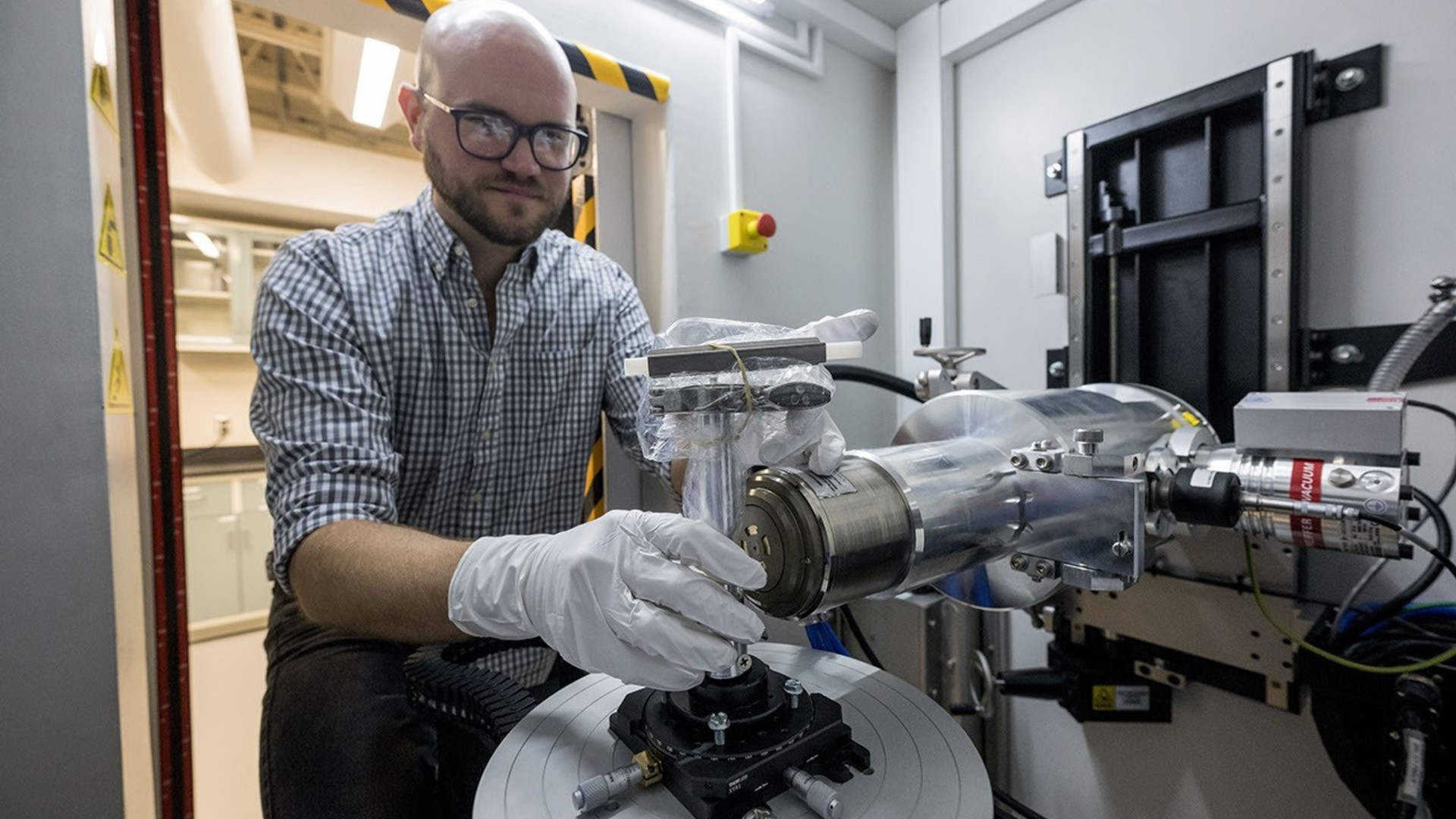 a person in rubber gloves operates a camera on the end of a metal arm inside a cleanroom