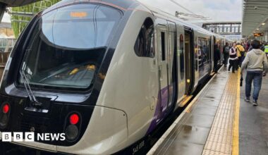 An Elizabeth line train at the platform with its doors open. There are people walking along the platform beside the train.