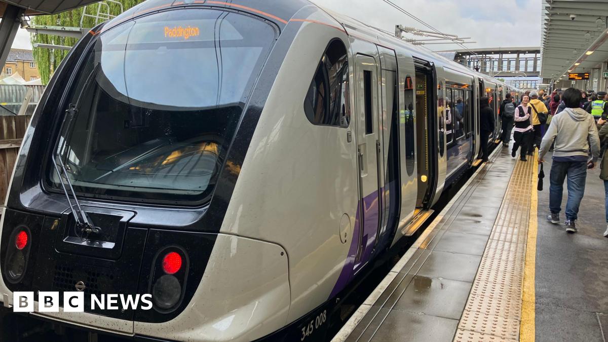 An Elizabeth line train at the platform with its doors open. There are people walking along the platform beside the train.