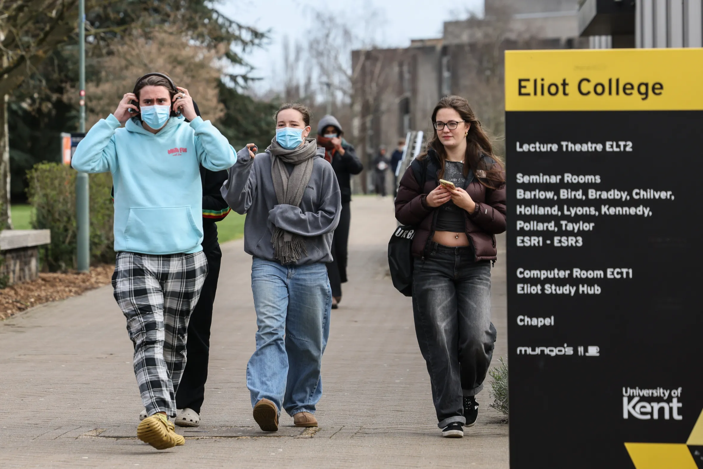 Students wearing facemasks walk past a sign for Eliot College at Kent University.