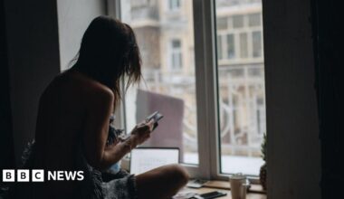 A woman in silhouette sitting in front of a window looking at her phone