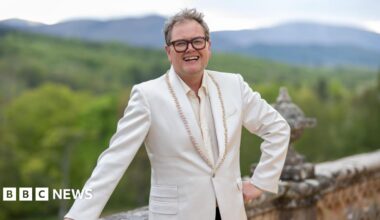 Alan Carr standing outside the Traitors castle in the Highlands