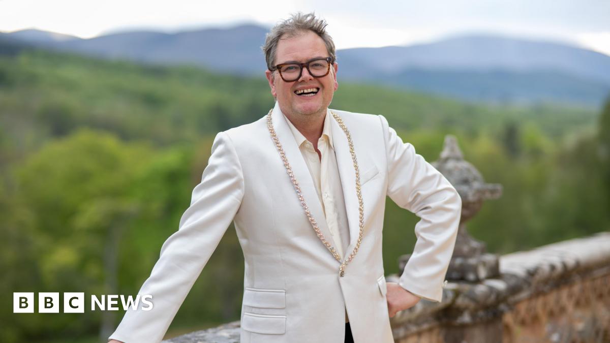 Alan Carr standing outside the Traitors castle in the Highlands
