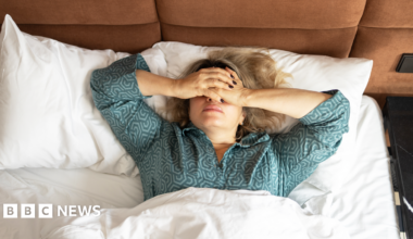 A women in green pajamas lies in bed with white bed linen photographed from above. She has her hands over her eyes.