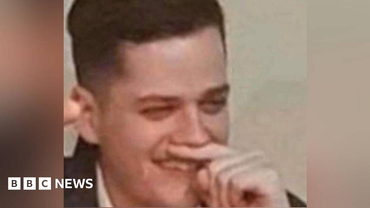 A man holds his finger under his nose while holding his right arm in the air