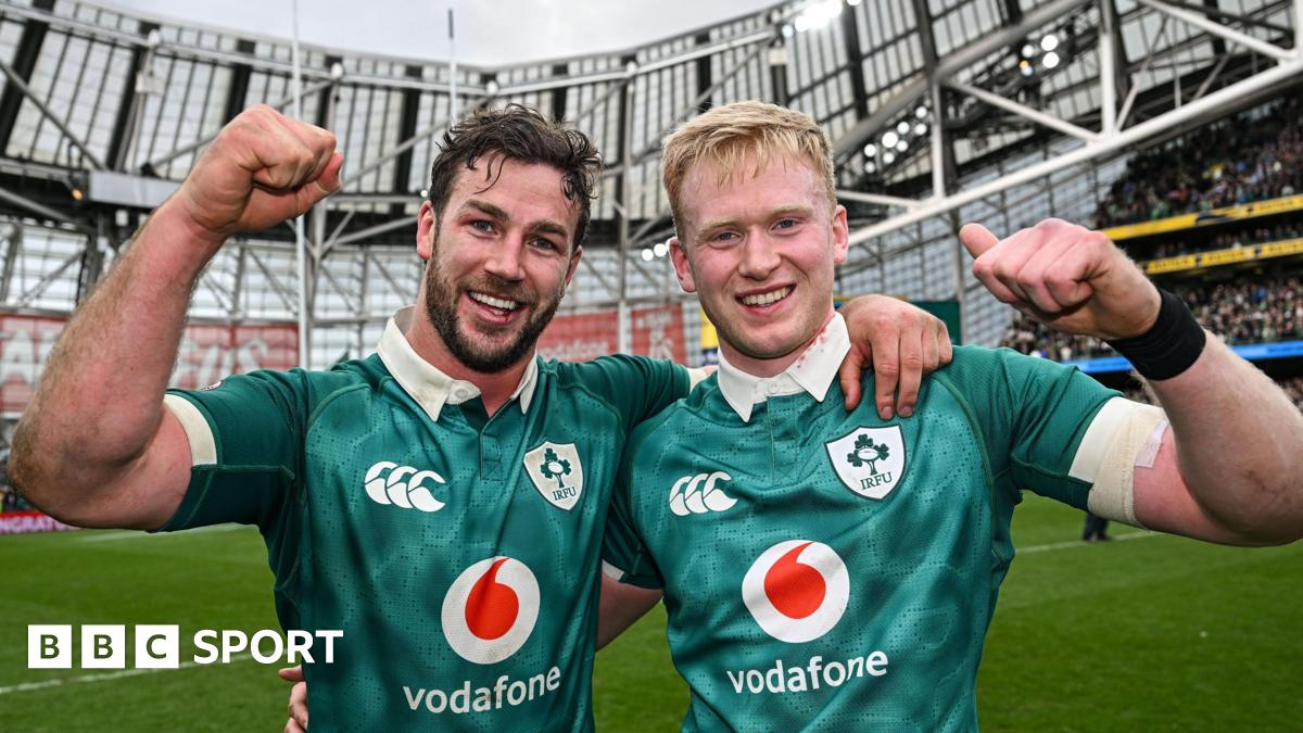 Caelan Doris and Jamie Osborne in a celebratory pose, arm in arm, with each man raising a clenched fist and smiling, while wearing Ireland's green shirt