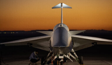 An aircraft resting on a section of runway as seen from the front, with its nose facing the camera. The early morning sky is orange in the background.