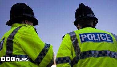 A back and side profile of two British Police officers wearing yellow high visibility jackets