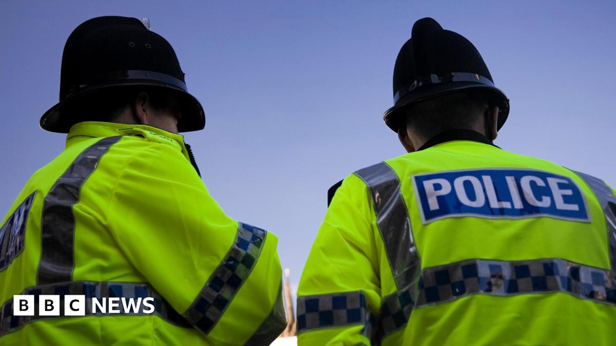 A back and side profile of two British Police officers wearing yellow high visibility jackets