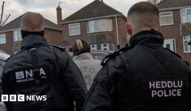 Two National Crime Agency officers arresting a woman in a residental area.