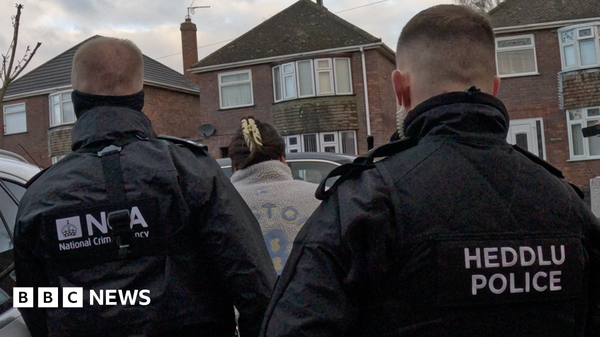 Two National Crime Agency officers arresting a woman in a residental area.