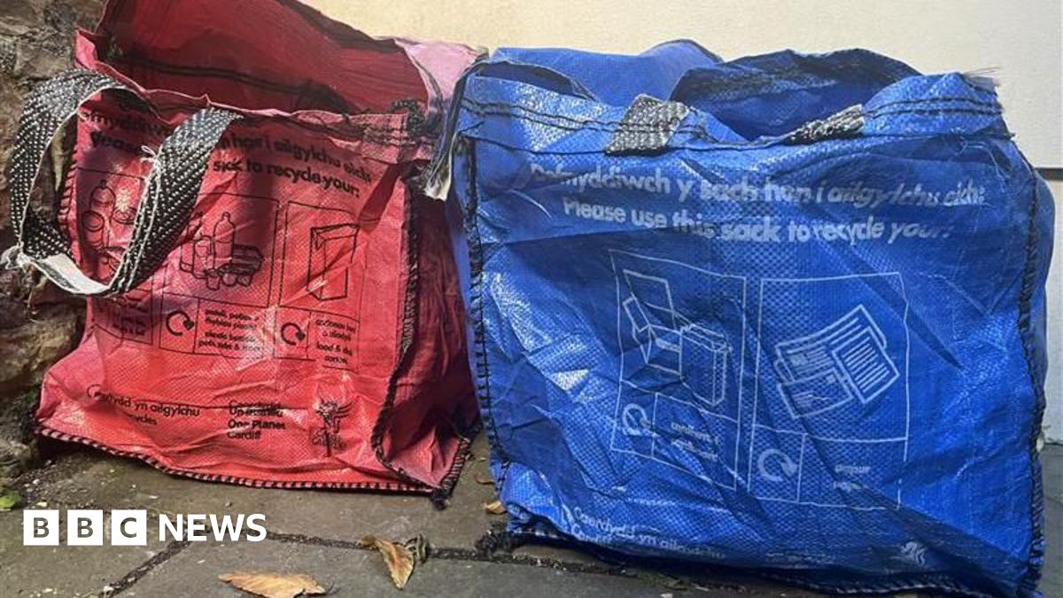 Two sacks, red and blue, pictured that are used for residents to separate their recycling. Sitting in front of a wall in garden.