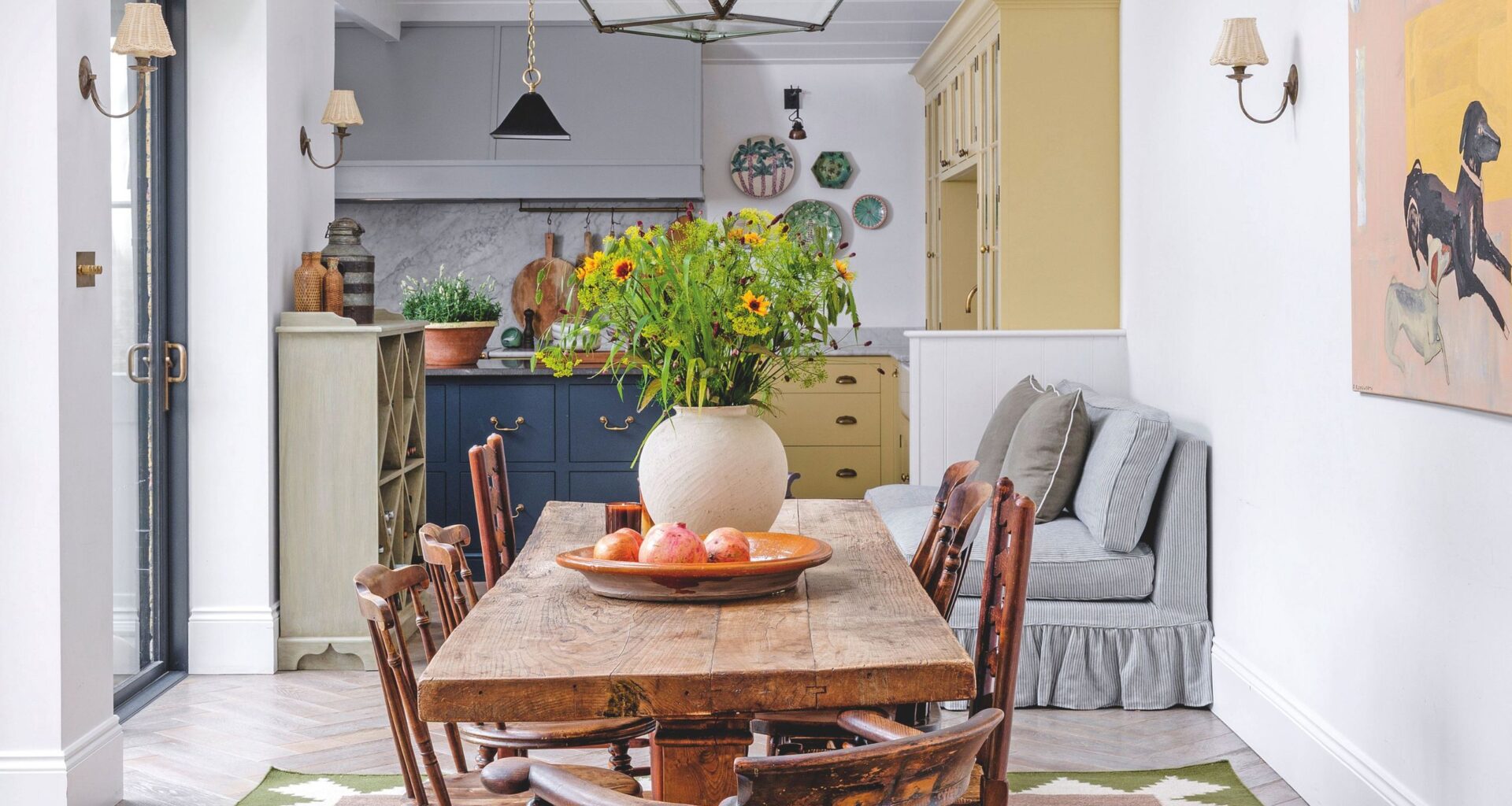 A bright, airy dining space with a rustic wooden table, antique spindle chairs, and a large glass lantern pendant light hanging from a vaulted white ceiling.