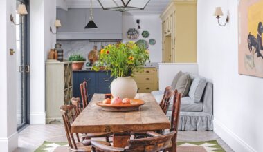 A bright, airy dining space with a rustic wooden table, antique spindle chairs, and a large glass lantern pendant light hanging from a vaulted white ceiling.