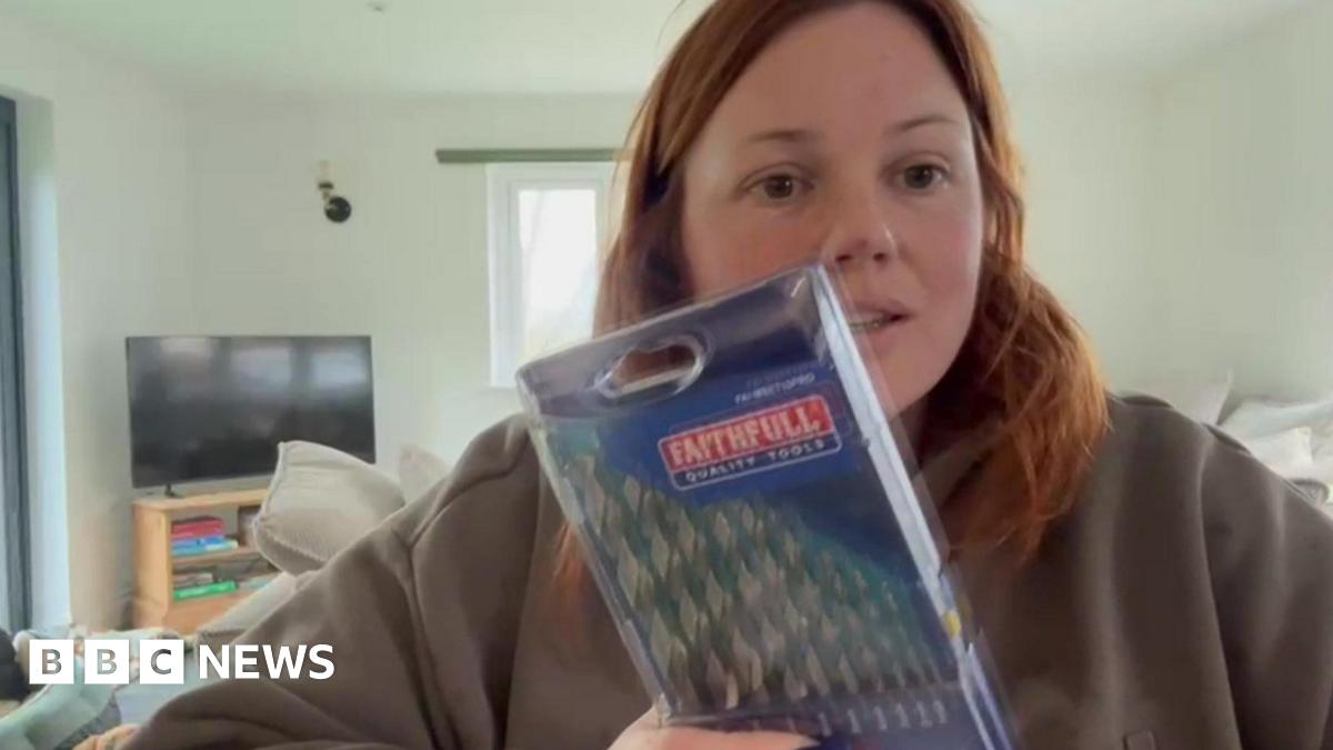 Megan Penny, who has red hair and is wearing a grey hoodie, is sat down showing the camera a packet of drill bits which she received instead of the phone she ordered.