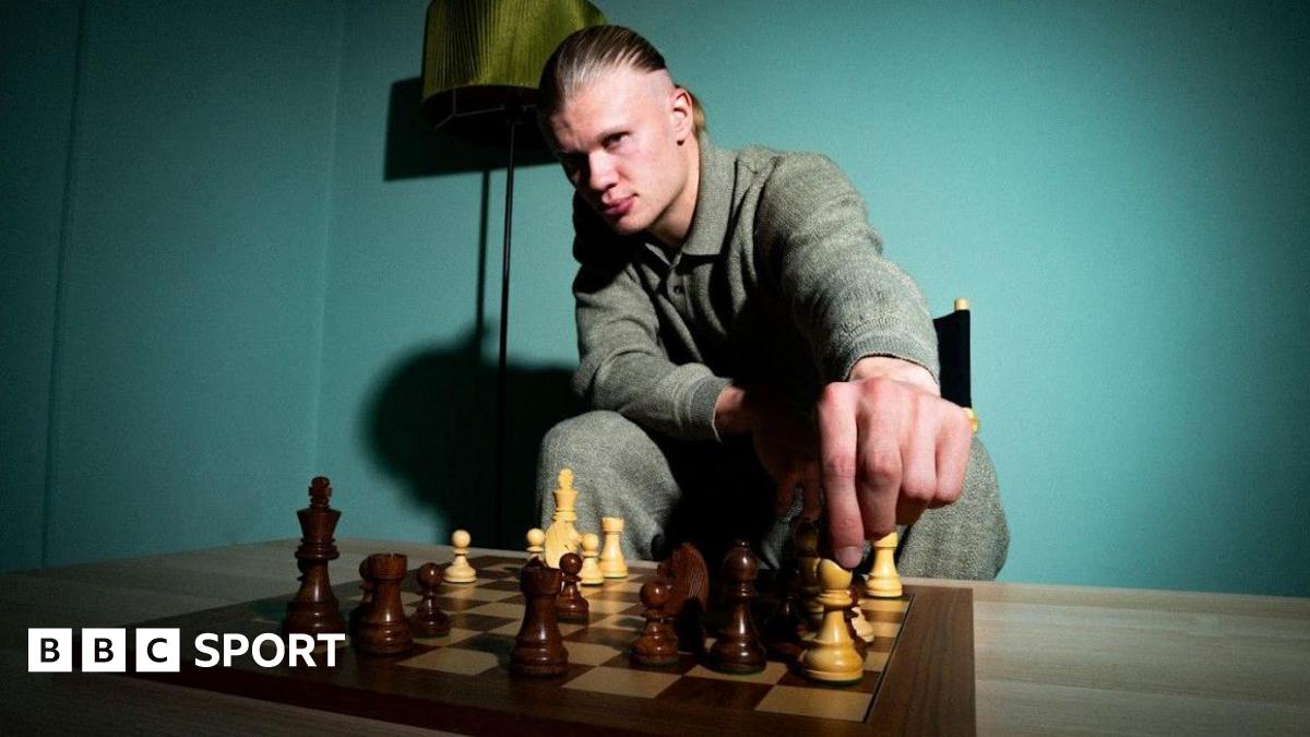 Erling Haaland looks into the camera as he moves a white bishop on a chess board.