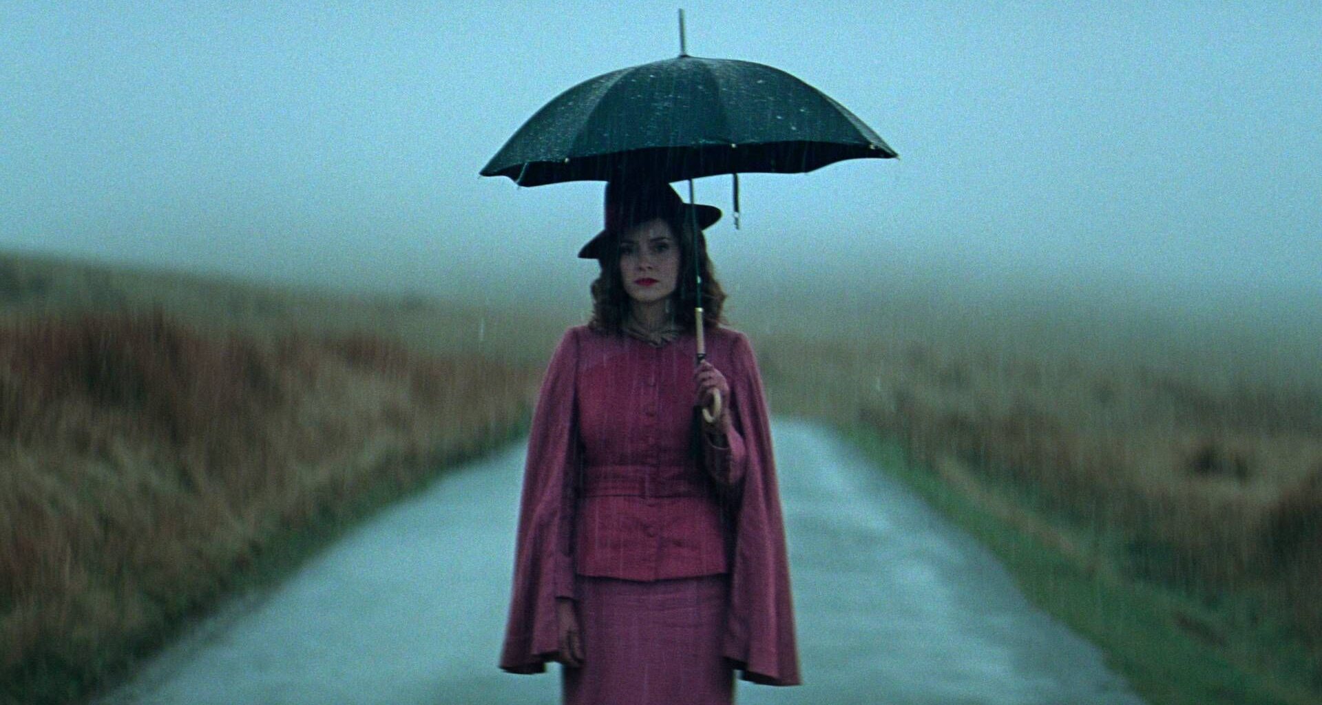 Sophie Rundle as Ada standing on the road and holding an umbrella in Peaky Blinders: The Immortal Man